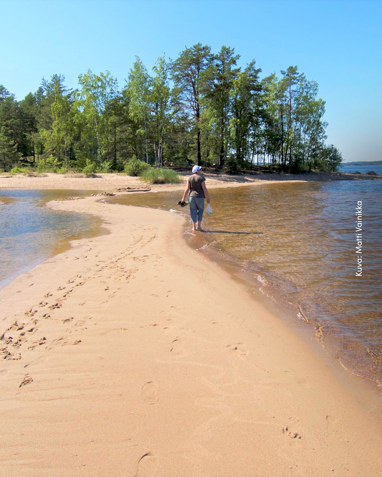 Nainen kävelemässä paljain jaloin rantahiekassa Rokan saarella.