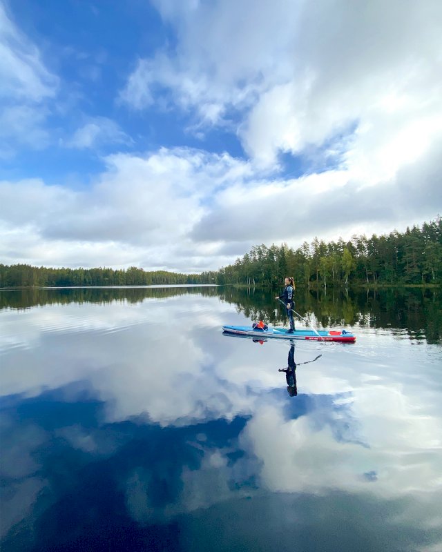 Nainen suppailee peilityynellä järvellä.