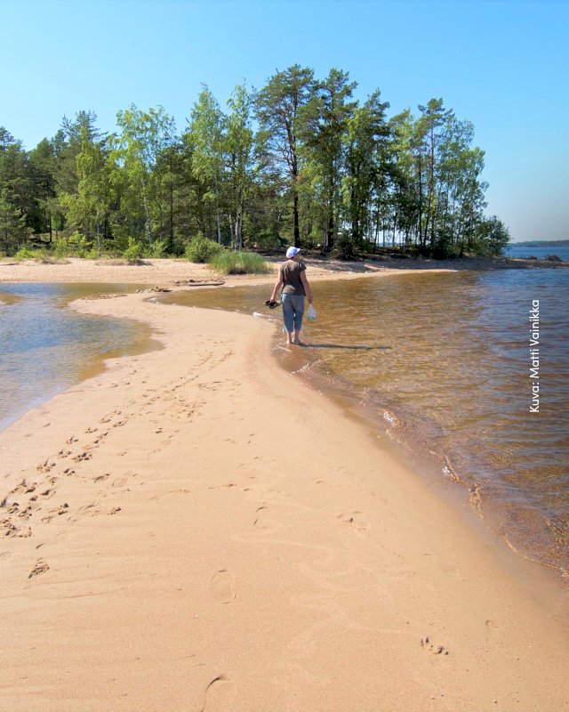 Nainen kävelemässä paljain jaloin rantahiekassa Rokan saarella.